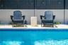Swimming pool with blue glass tile waterline, stone-paved decking, light-toned masonry perimeter wall, and dark-finished vertical board fencing