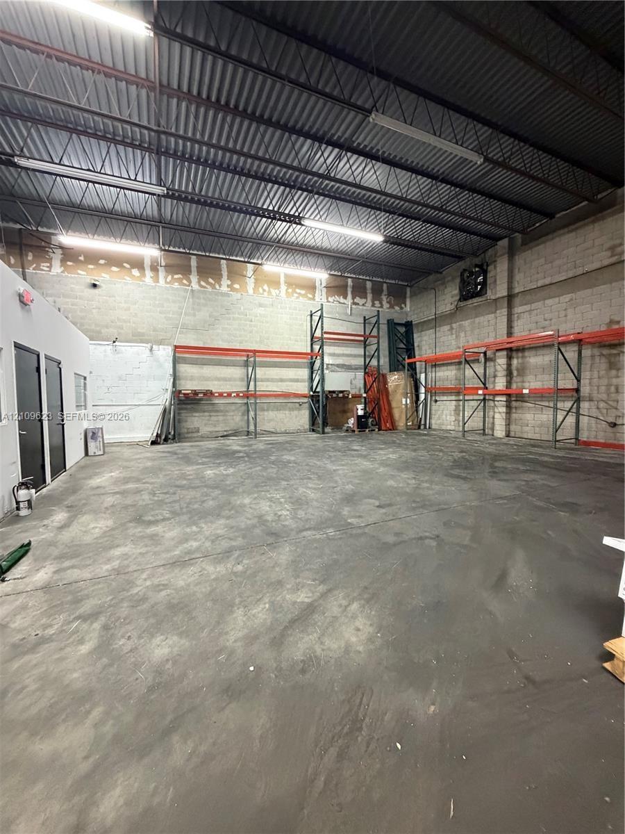 Open-concept industrial warehouse space featuring high ceilings with exposed steel trusses, polished concrete flooring, concrete block walls, and inte