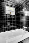 Full-height black square tile surround, white soaking tub, chrome multi-handle faucet assembly, adjustable chrome shower head, and an operable window