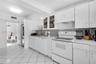 Kitchen featuring white cabinetry with glass-front display uppers, mosaic tile backsplash, solid-surface countertops, tile flooring, and integrated wh