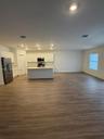 Open-concept kitchen featuring white shaker cabinetry, a center island with a solid surface countertop, wood-finish flooring, and stainless steel appl