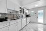 Kitchen featuring white cabinetry with glass-front display uppers, mosaic tile backsplash, solid-surface countertops, dual-basin stainless steel sink 