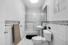 Bathroom featuring white tile flooring, pedestal sink, tub-shower combination with sliding glass doors, and decorative tile accent wall detailing
