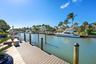 Waterfront property featuring a private boat dock, wooden decking, stone-tiled patio, and mature palm trees