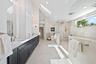 Double vanity with dark cabinetry, stone-finish countertops, skylights, vaulted ceiling, and a walk-in shower with stone tile surround