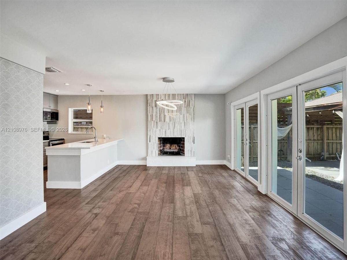 Open-concept interior featuring wood-finish flooring, floor-to-ceiling fireplace with vertical stone-finish surround, kitchen island with solid-surfac
