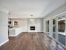Open-concept interior featuring wood-finish flooring, floor-to-ceiling fireplace with vertical stone-finish surround, kitchen island with solid-surfac