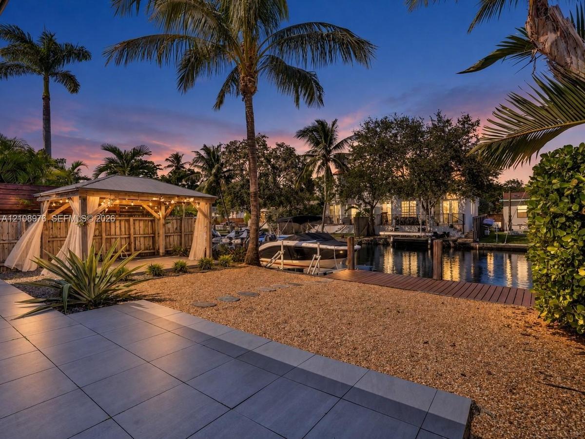 Waterfront property featuring a covered timber-framed gazebo, wooden dock, gravel landscaping, and large-format tile patio