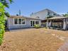 Rear exterior featuring a concrete patio, stone paver path, wood-frame gazebo, and gravel landscaping