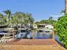 Waterfront canal property featuring a wooden boat dock, mature landscaping, and structural seawall