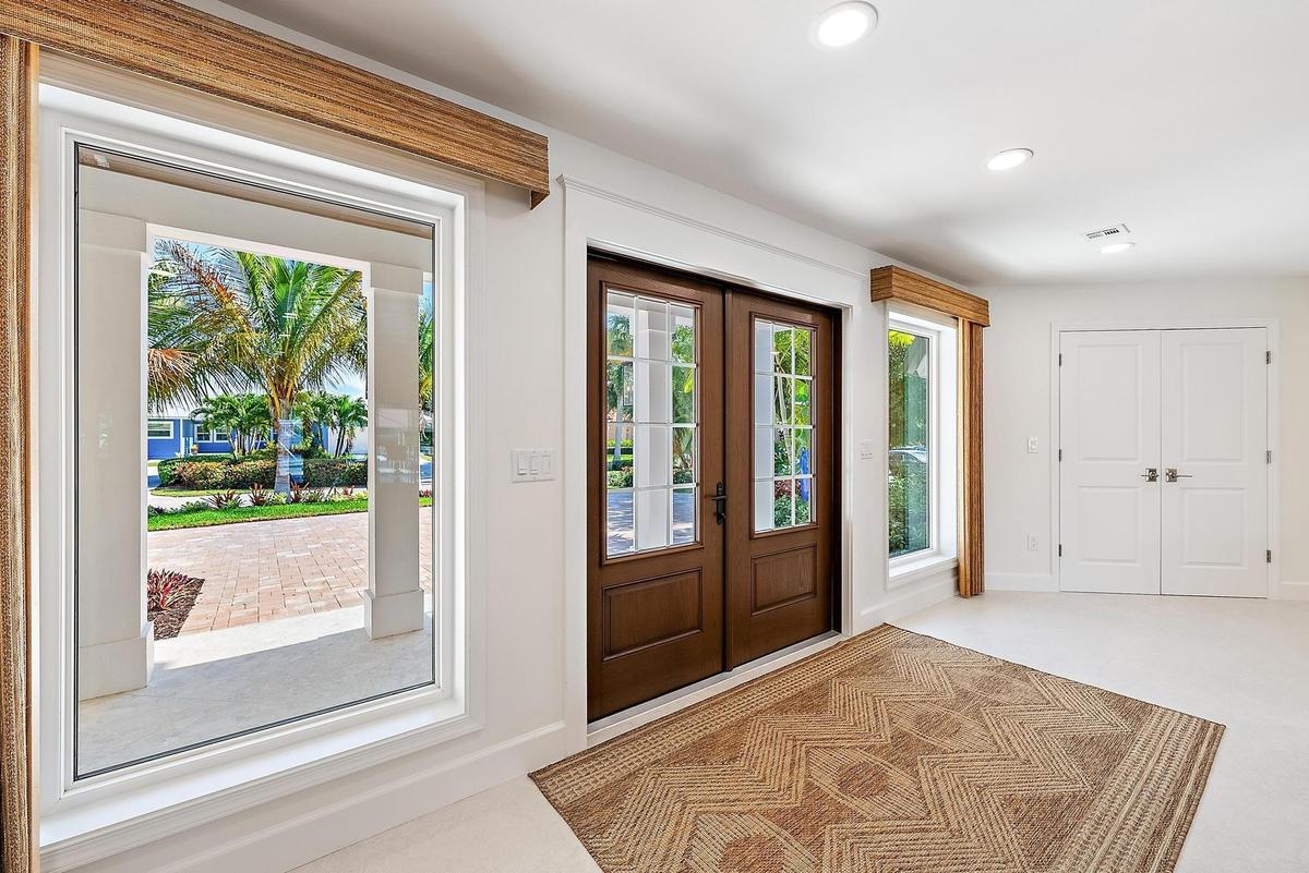 Double entry doors with divided-lite glass panels, neutral tile flooring, recessed ceiling lighting, and large picture windows featuring wood-finish v