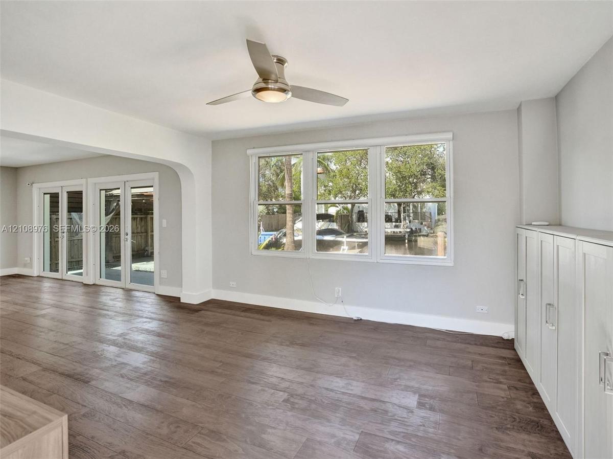 Open living area featuring wood-finish flooring, a contemporary ceiling fan with integrated lighting, triple-pane window configuration, and built-in w