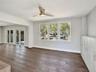 Open living area featuring wood-finish flooring, a contemporary ceiling fan with integrated lighting, triple-pane window configuration, and built-in w