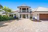 Two-story exterior featuring a metal roof, paver driveway, double-door entrance, second-story balcony, and multi-car garage with wood-finish door