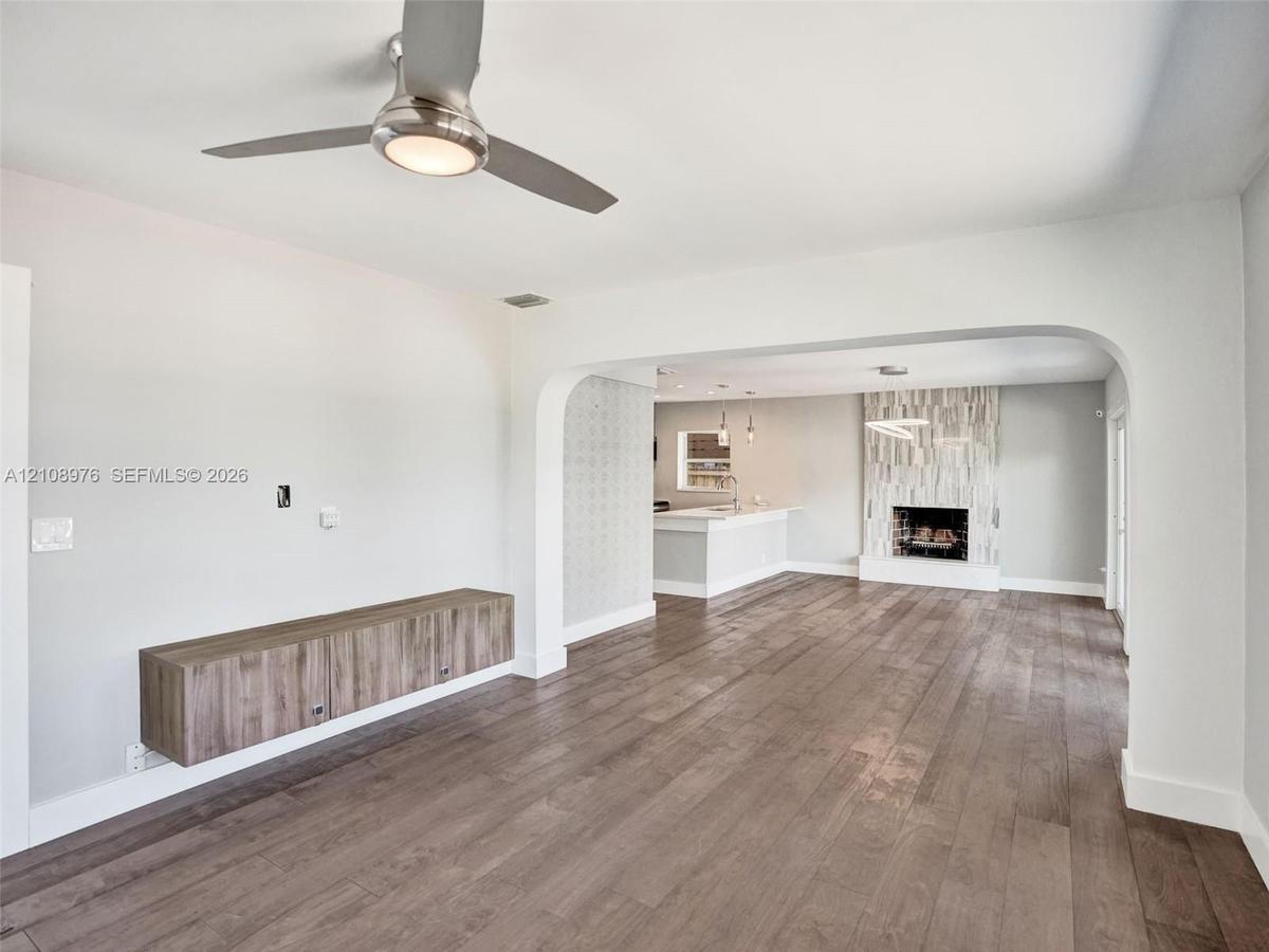 Wood-finish flooring, brushed-nickel ceiling fan with integrated lighting, wall-mounted wood-finish cabinetry, arched entryway, and fireplace with ver