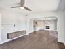 Wood-finish flooring, brushed-nickel ceiling fan with integrated lighting, wall-mounted wood-finish cabinetry, arched entryway, and fireplace with ver