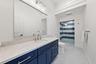 Navy blue vanity with light-toned stone countertop, integrated sink, expansive wall-mounted mirror, and walk-in shower with horizontal tile pattern