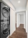 Laundry area featuring a stackable stainless steel appliance unit, recessed lighting, and wood-finish flooring