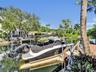 Waterfront bulkhead featuring a boat lift, concrete seawall, and tropical landscaping