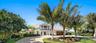 Two-story exterior featuring a metal roof, balcony with decorative railings, multi-car garage, and a paved circular driveway surrounded by mature palm