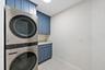 Laundry area featuring custom blue shaker-style cabinetry, stone-surface countertop, and stainless steel stacked appliance unit