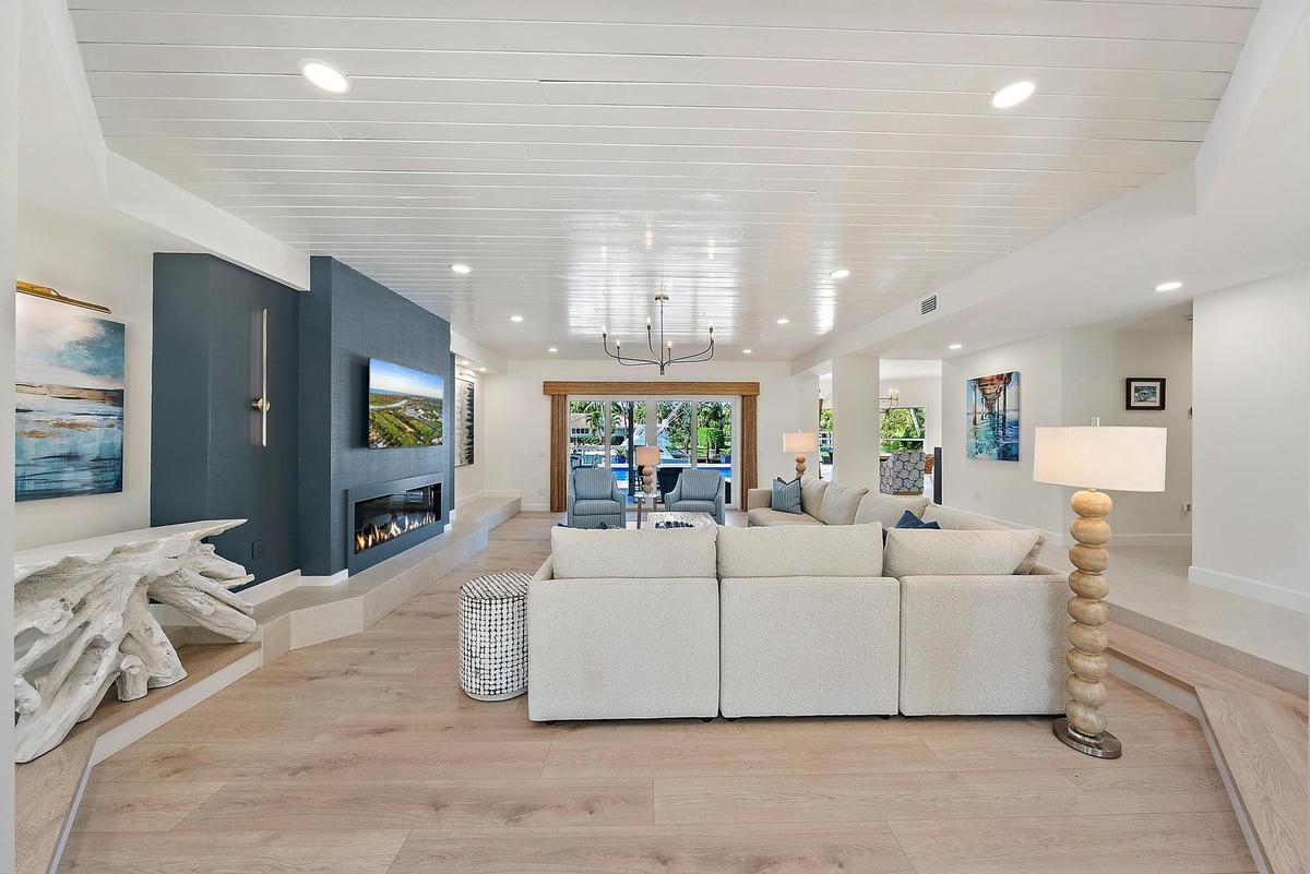 Living area featuring a shiplap ceiling, wood-finish flooring, a tiered floor design, a built-in linear fireplace, and an accent wall