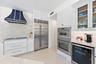 Kitchen featuring white cabinetry, custom range hood, integrated stainless steel refrigerator, built-in double wall ovens, and stone countertops