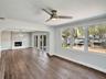 Wood-finish flooring, fireplace with vertical tile surround, recessed ceiling fan with integrated lighting, and multiple windows with water frontage