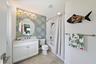 Bathroom featuring a white vanity cabinet with a stone-surface countertop, scalloped-edge wall mirror, four-light vanity fixture, and a tub-shower com