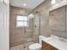 Walk-in shower with sliding glass door, mosaic floor tiling, full-height wall tile, wood-finish vanity with stone countertop, and recessed ceiling lig