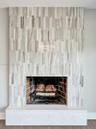 Fireplace featuring floor-to-ceiling vertical tile surround, brick-lined firebox, metal grate, and a solid rectangular hearth