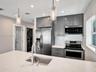 Kitchen featuring grey shaker-style cabinetry, white stone-finish countertops, stainless steel appliances, mosaic tile backsplash, and glass pendant l