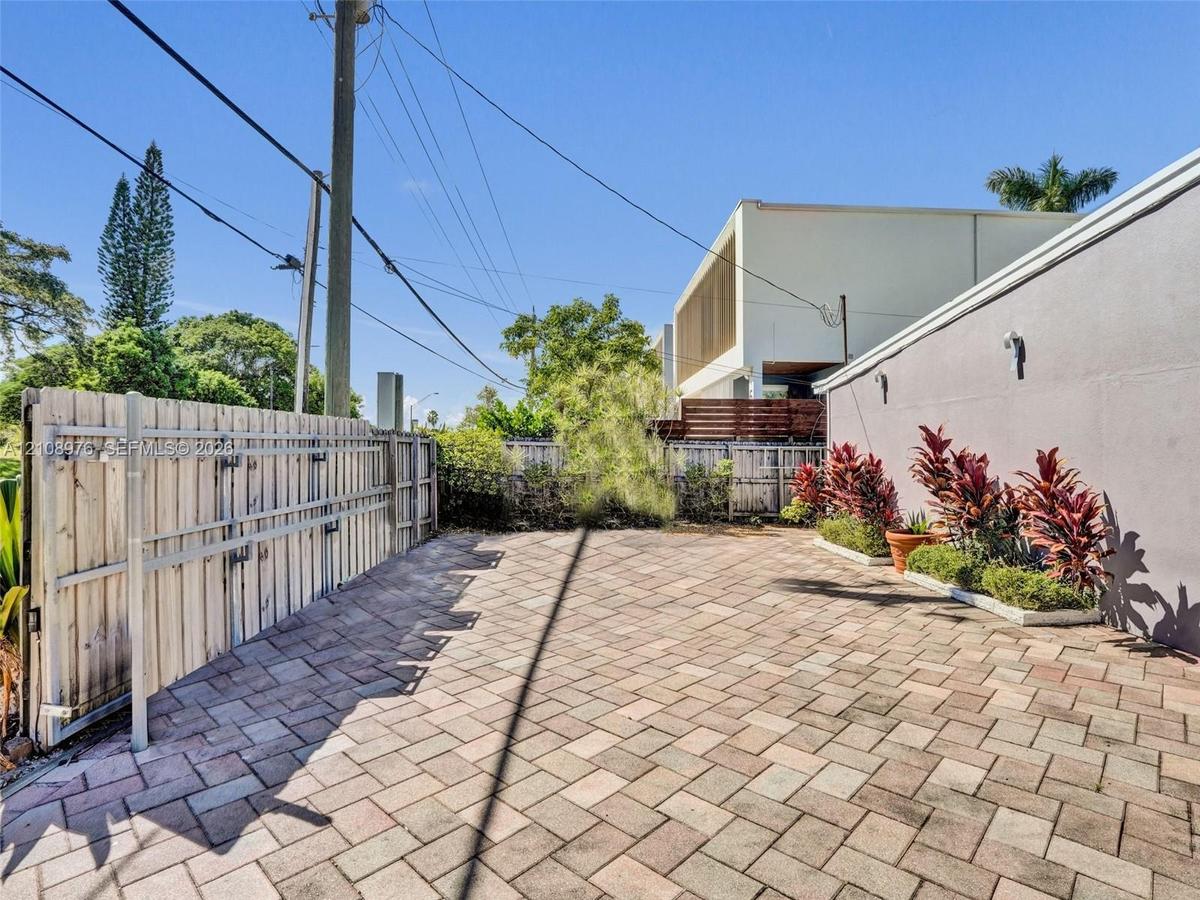 Paved courtyard featuring herringbone-patterned stone pavers, perimeter wood privacy fencing, and a dedicated planting bed