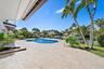 Waterfront patio featuring stone paver hardscaping, a custom-shaped swimming pool, built-in metal pool railings, and mature palm landscaping