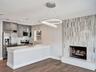 Kitchen featuring grey cabinetry, stainless steel appliances, and a peninsula with a quartz countertop, complemented by a floor-to-ceiling fireplace w