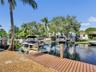 Waterfront canal property featuring a private wood-plank dock, boat lift, gravel landscaping, and mature palm trees