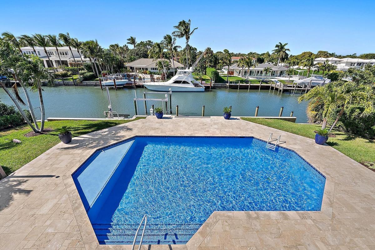 Waterfront property featuring a private boat dock, in-ground swimming pool, stone-paver deck, and manicured lawn