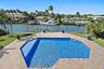 Waterfront property featuring a private boat dock, in-ground swimming pool, stone-paver deck, and manicured lawn