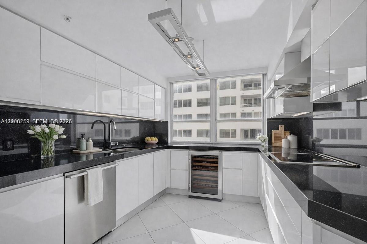 Kitchen featuring high-gloss white cabinetry, dark stone countertops, stainless steel appliances, a built-in wine cooler, and a linear pendant light f
