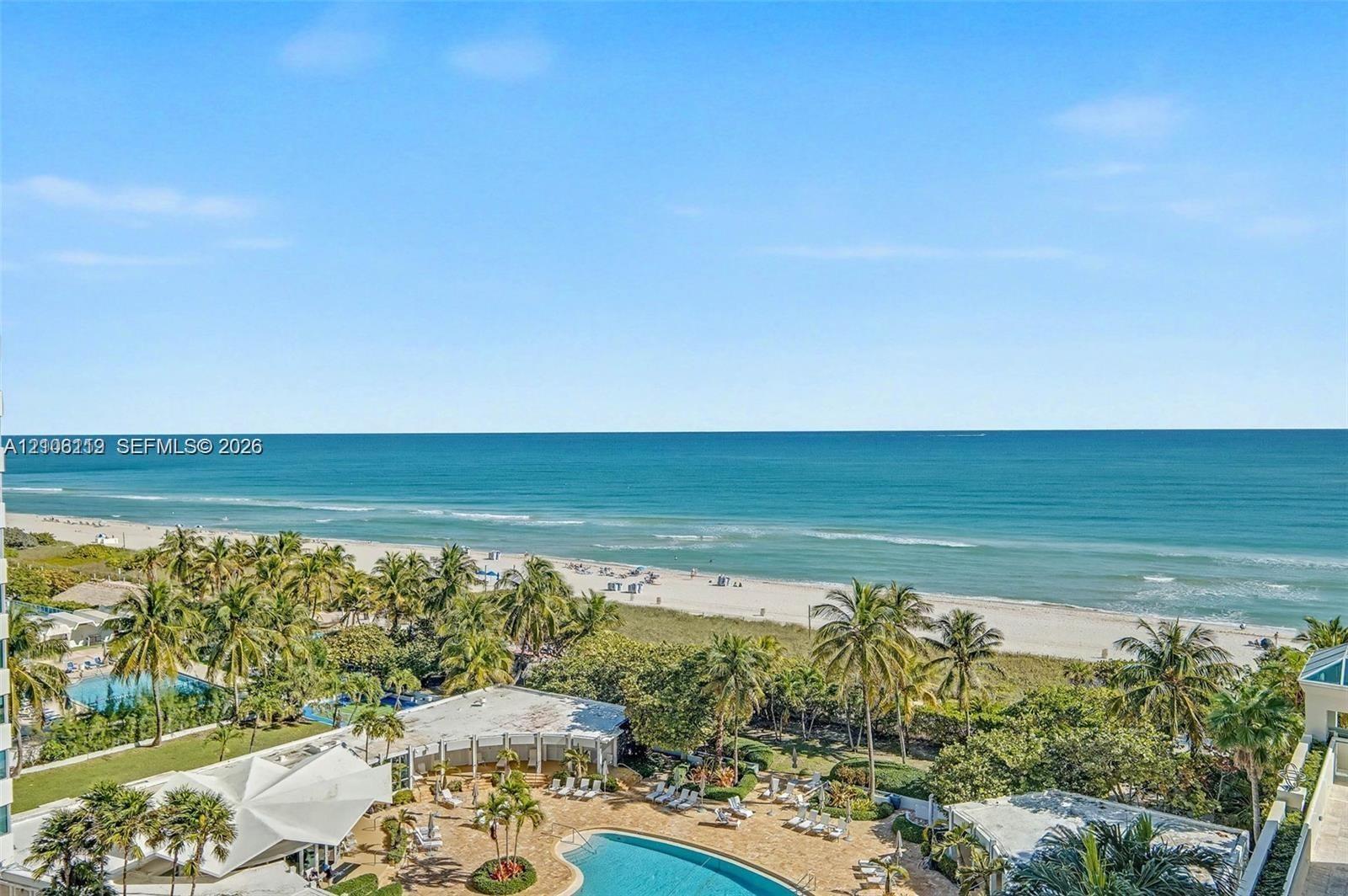 Elevated perspective featuring direct oceanfront access, sandy beach frontage, mature palm trees, and an expansive outdoor swimming pool with surround