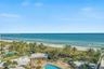 Elevated perspective featuring direct oceanfront access, sandy beach frontage, mature palm trees, and an expansive outdoor swimming pool with surround