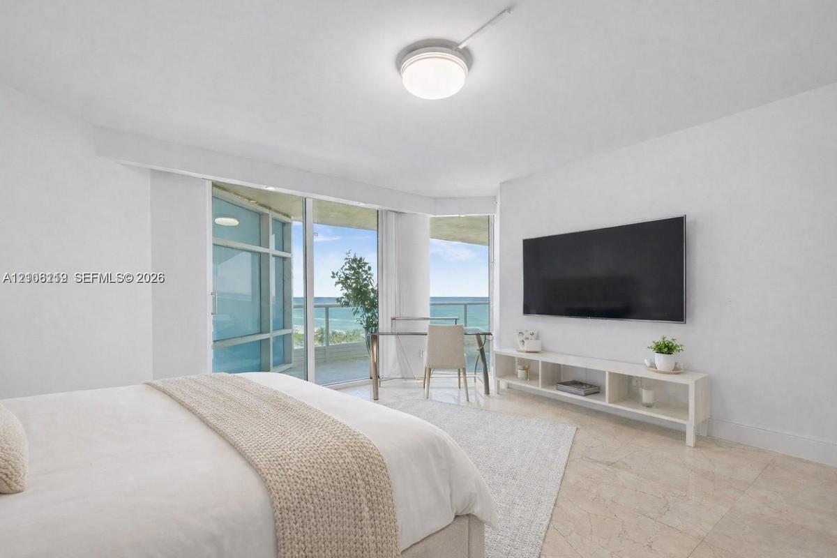 Floor-to-ceiling glass sliders, stone tile flooring, circular flush-mount ceiling light, and coastal ocean horizon