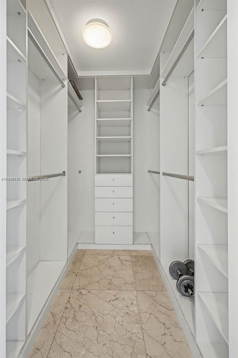 Walk-in closet featuring white built-in shelving, integrated dresser drawers, hanging rods, and natural stone flooring