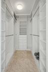 Walk-in closet featuring white built-in shelving, integrated dresser drawers, hanging rods, and natural stone flooring