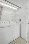 Laundry area featuring white ceramic wall tiling, stone-finish flooring, built-in wall-mounted drying rack, and white shaker-style doors