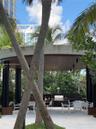 Outdoor pavilion featuring a circular concrete roof, wood-plank ceiling, black support columns, built-in stone-finish grill station, and stone-tile pa