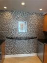 Multi-tonal mosaic tile wall, integrated black stone counter, recessed ceiling lighting, and polished wood-finish cabinetry