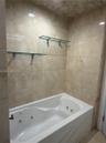 Jetted bathtub featuring full-height natural stone wall tiling and two integrated glass shelving units