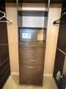 Custom built-in closet organization system featuring dark wood-finish cabinetry, four integrated storage drawers, vertical shelving, and metallic hard