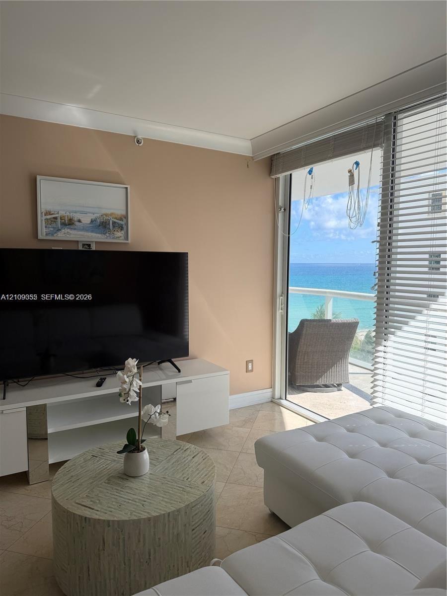 Living area featuring tile flooring, floor-to-ceiling glass sliding doors, and a balcony with an ocean backdrop
